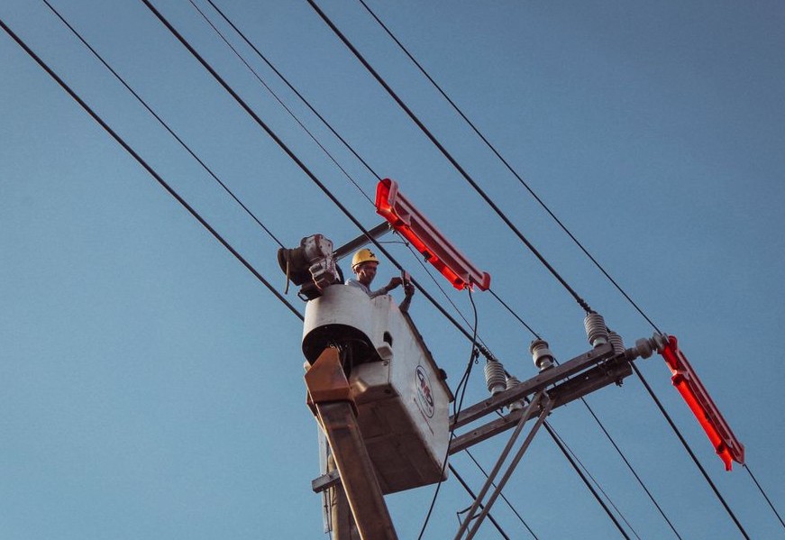Electrician in a lift repairing overhead power lines on a clear day