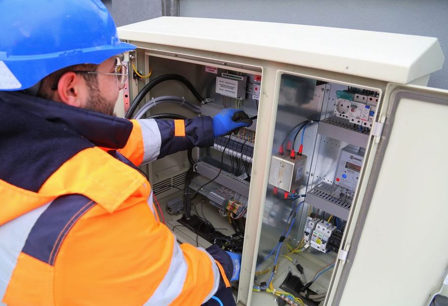 Engineer in safety gear working on an outdoor electrical panel, ensuring system functionality
