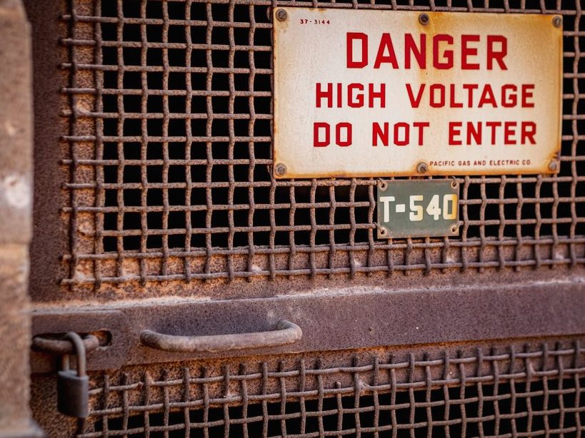 Close-up of a rusty industrial gate with a high voltage warning sign, conveying danger